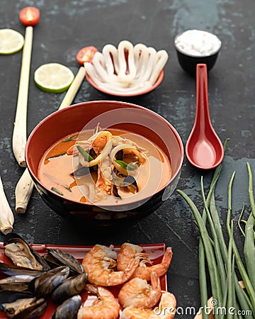 Exotic noodle and mussel soup with seafood. Clay bowl of spicy oriental dish and ingredients for making it on black Stock Photo