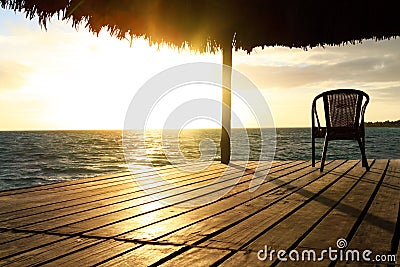 Exotic wooden gazebo and chair on the beach at sunset or sunrise. Background of a seashore with seat, resting pavilion, palm trees Stock Photo