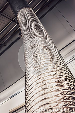 Expandable metallic air-conditioning ventilation pipe or tube rising up to the ceiling inside a grey industrial type unit Stock Photo