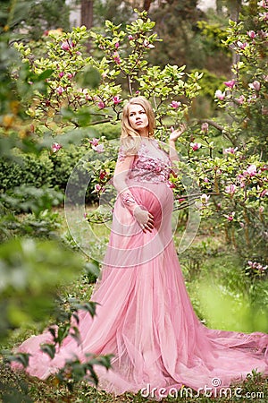 Expectant mother in beautiful long dress in garden near blooming magnolia Stock Photo