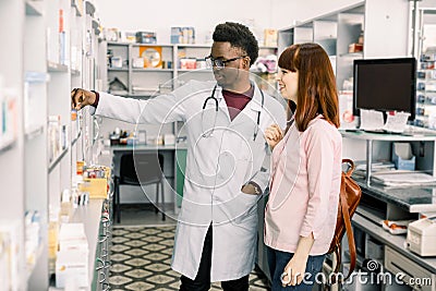 Experienced African American man pharmacist consulting female customer in modern pharmacy Stock Photo