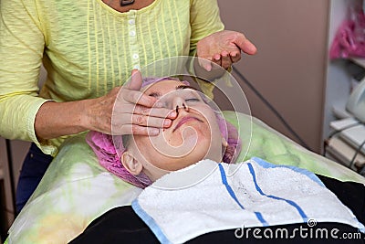 An experienced cosmetologist applies a mask of emulsion on the face of a young girl who lies on the couch during facial cleansing Stock Photo