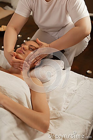 Experienced resolute masseuse in white uniform processing face Stock Photo