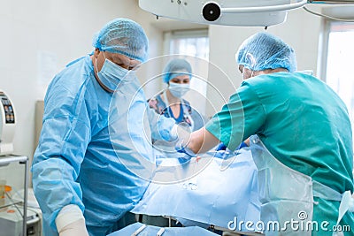An experienced surgeon in a mask and gown operates in a sterile operating room with an assistant and an anesthesiologist..A group Editorial Stock Photo