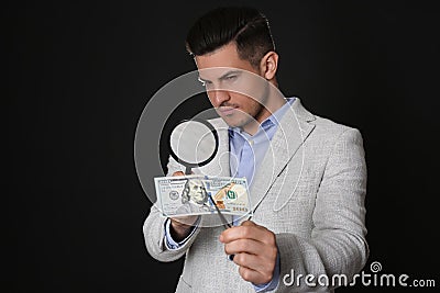 Expert authenticating 100 dollar banknote with magnifying glass against black background. Fake money concept Stock Photo