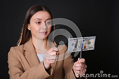 Expert authenticating 100 dollar banknote with magnifying glass against black background, focus on hand. Fake money Stock Photo