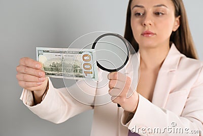 Expert authenticating 100 dollar with magnifying glass against light grey background, focus on hand. Fake money concept Stock Photo