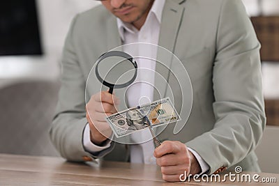 Expert authenticating 100 dollar banknote with magnifying glass at table in office, closeup. Fake money concept Stock Photo