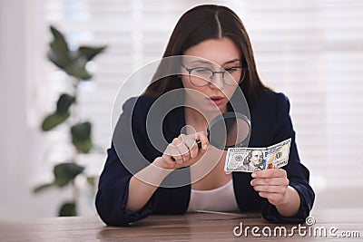 Expert authenticating dollar banknote with magnifying glass at table in office, focus on hand. Fake money concept Stock Photo