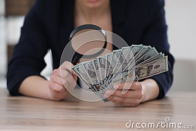 Expert authenticating 100 dollar banknotes with magnifying glass at table in office, closeup. Fake money concept Stock Photo