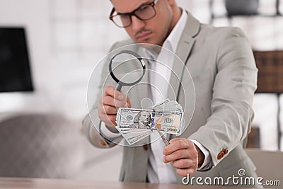 Expert authenticating 100 dollar banknotes with magnifying glass at table in office, focus on hand. Fake money Stock Photo