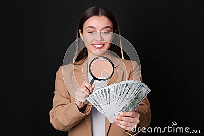 Expert authenticating 100 dollar with magnifying glass against black background, focus on hand. Fake money concept Stock Photo