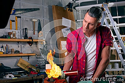 Expert carpenter burning a wood leg with a professional gas burner. Flames and smoke, fire and timber. Portrait of Stock Photo
