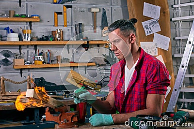 Expert carpenter burning a wood leg with a professional gas burner. Flames and smoke, fire and timber. Portrait of Stock Photo
