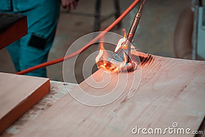 Expert carpenter burning a wood slab with a professional gas burner. Flames and smoke, fire and timber. Stock Photo