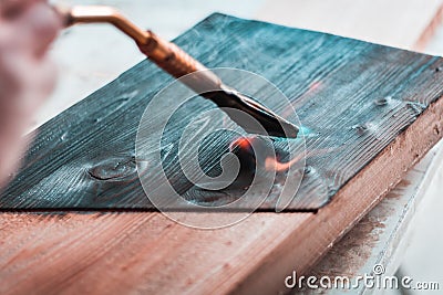 Expert carpenter burning a wood slab with a professional gas burner. Flames and smoke, fire and timber. Stock Photo
