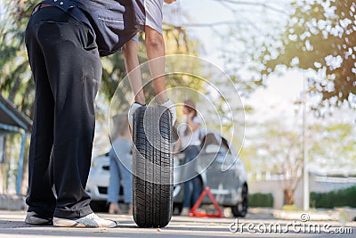 Expertise mechanic man in uniform holding a tire for help a woman for changing car wheel on the highway, car service, repair, Stock Photo