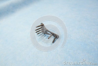 explanted titanium plate and 4 titanium screws for the treatment of a radius fracture are lying on a light blue support Stock Photo