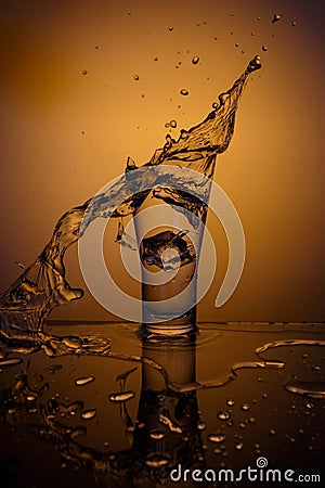 Exploding Glass cup with water shattering over orange background. Stock Photo