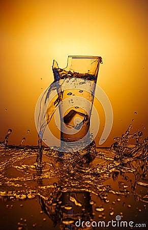Exploding Glass cup with water shattering over orange background. Stock Photo
