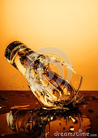 Exploding Glass cup with water shattering over orange background. Stock Photo