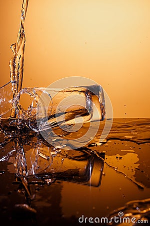 Exploding Glass cup with water shattering over orange background. Stock Photo