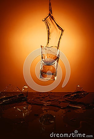 Exploding Glass cup with water shattering over orange background. Stock Photo