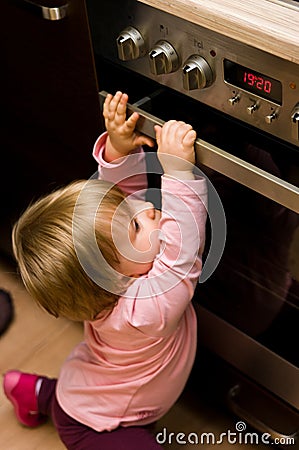 Toddler gripping kitchen oven door Stock Photo