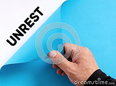 Exposing the hidden unrest concept. Male hand opens the blue paper and reveals the word unrest Stock Photo