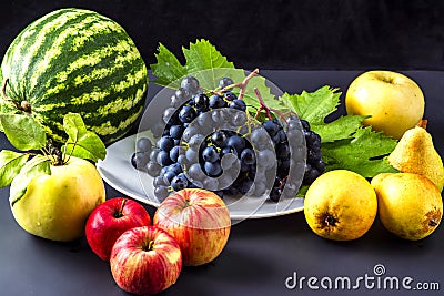 Exposition of fresh natural fruits, healthy food with many vitamin, watermelon, apple, grapes, pears on black background. Stock Photo