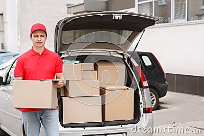 Express delivery to home. Courier holds box near open car with parcels Stock Photo