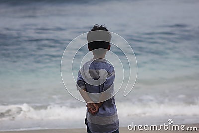 the expression of a child dressed in a blue striped shirt who is enjoying the beach view and wants to play in the sand Stock Photo