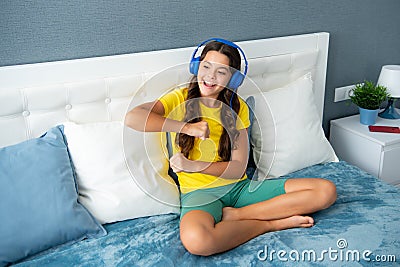 Expressive emotional excited teen girl. Teenager girl in headphones relax on bed at home using headphones, singing and Stock Photo