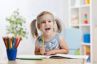 Expressive kid girl draws sitting at table in room in nursery Stock Photo