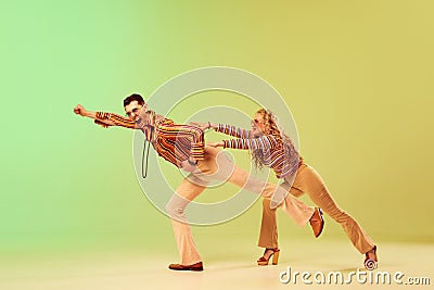 Expressive, talented young couple, man and woman in stylish vintage costumes dancing against gradient green yellow Stock Photo