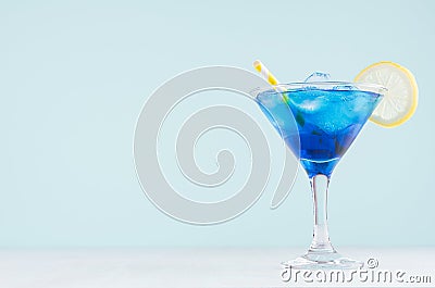Exquisite blue cocktail for celebration in beach style with blue curacao, ice cube, lemon slice, yellow straw in mint color bar. Stock Photo