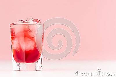 Exquisite cold red alcoholic liquor with ice cubes in shot glass closeup on white wood table and pastel pink wall, copy space. Stock Photo