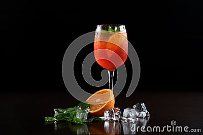 Cocktail glass with cold drink, slices of grapefruit, mint leaves and ice on black background. Stock Photo