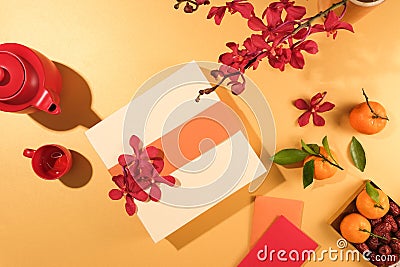 An exquisite gift box, tangerines, a tea set, lucky money envelopes, and vibrant red orchids take center stage on a pastel Stock Photo