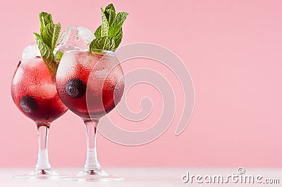 Exquisite red alcoholic shots of sweet berry liquor with ice cubes, blueberry, green mint on pastel soft light pink background. Stock Photo