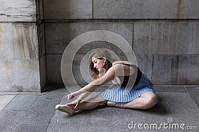 Ballerina sitting in profile on stone porch stretching over her pointe shoes Stock Photo