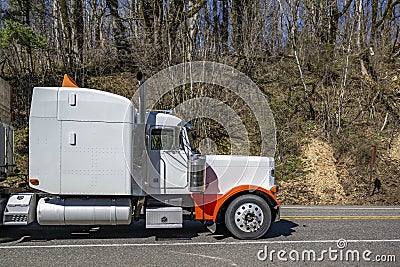 Extended cab white big rig bonnet semi truck with orange accents transporting wood boxes on flat bed semi truck running on the Stock Photo