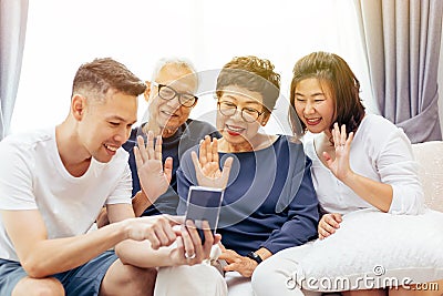 Extended family making a video call and waving at the caller. Asian multi generation family with senior and young couple together Stock Photo