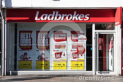 Exterior shot of Ladbrokes Gambling Betting Shop on High Street with adverts in window Editorial Stock Photo