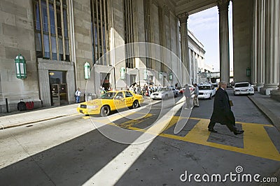 Exterior view of yellow taxi cab and walking business man in front of the 30th Street Station, a national Register of Historic Pl Editorial Stock Photo