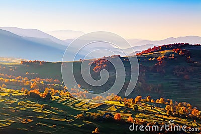 Extraordinary autumn scenery. Green fields with haystacks. Trees covered with orange and crimson leaves. Mountain landscapes. Stock Photo