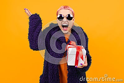 Extraordinary beautiful woman with short pink hair in dark coat and glasses holds a white box with gift and rejoices Stock Photo