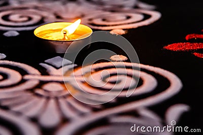 Extreme close up of glowing tea lamp and white red rangoli art on black background. diwali concept Stock Photo