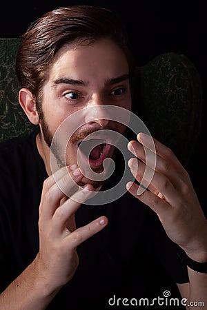 Extreme close up of young adult male mouth open, both hands up in shock or surprise. Deep color tones for dramatic effect, dark Stock Photo