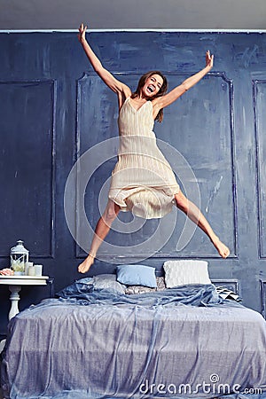 Extremely excited woman in nightgown jumping on bed with arms an Stock Photo